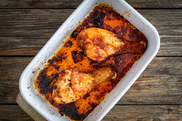 Baked chicken drumsticks in baking dish on wooden table. Top view