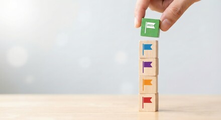 Close up of an adult hand stacking wooden blocks with colorful flags indoors to plan 2023 business goals and milestones, representing successful strategic growth and progress in a bright office.