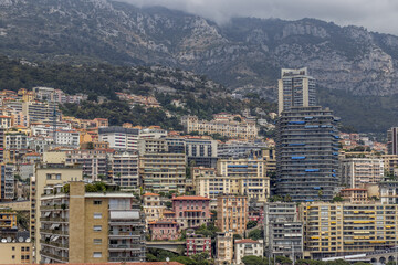 View of densely packed architecture rises in a symphony of colors and textures, nestled under the watchful gaze of cloud-veiled mountains, Monaco, Monaco.