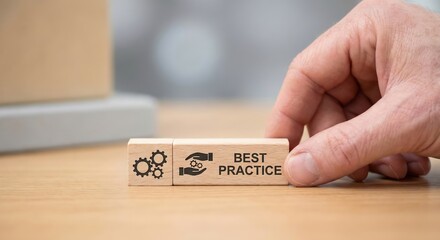 Close-up of a Caucasian adult hand placing wooden blocks featuring best practice and gear icons on a desk in a bright office, representing business strategy, excellence, and process improvement.