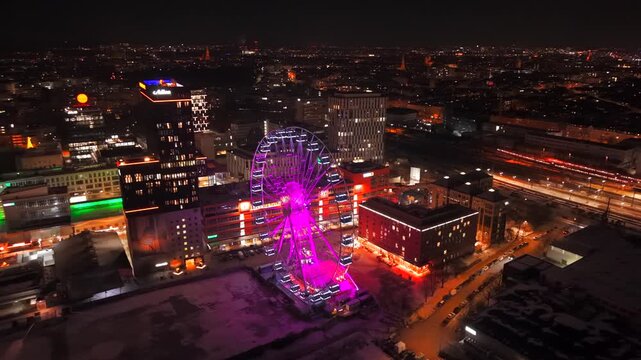 Drone video from above of Munich East at night. Umadum Ferris Wheel and illuminated city lights define the Werksviertel-Mitte skyline in Bavaria. Luftaufnahme Riesenrad nahe Muenchner Ostbahnhof 