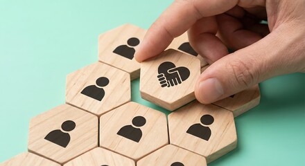 Adult woman hand placing a wooden hexagon block with heart handshake icon into a cluster of team member icons, representing community, trust, partnership, and human resources collaboration.