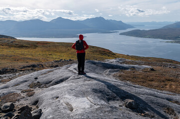 Fototapeta premium Young woman hiker standing on top of a mountain overlooking the Arctic city of Tromso and Norwegian fjords in autumn.