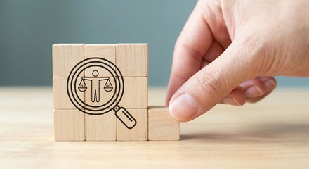 Adult woman hand placing a wooden block to complete an ethics and justice icon with a magnifying glass for corporate compliance, audit, and moral decision making in a bright minimalist office.