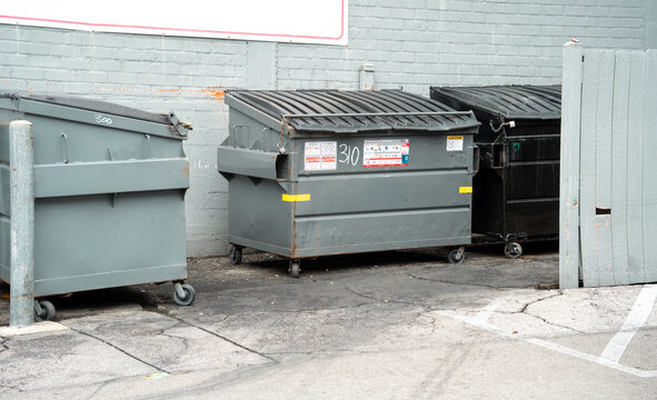 Commercial dumpsters lined up against a brick wall in an urban alleyway setting