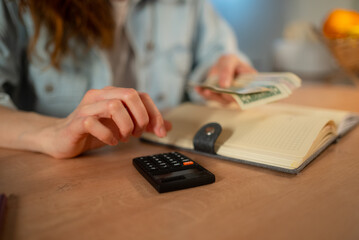 Person's hands organizing cash, using a calculator, and reviewing a notebook for budgeting and payment of utility bills, emphasizing financial planning and money management