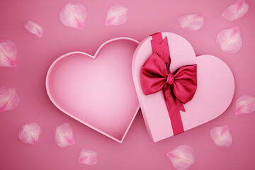 Open heart shaped present box wrapped with red bow tie and rose flower petals on pink background. Valentine's day giftbox for luxury product mockup. Mother's day, woman, birthday, anniversary holiday