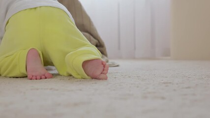 Baby engaged in persistent crawling exercise at home. Adorable infant patiently practicing crawling on carpet. Infant begins early mobility close up. Neutral tones of the nursery and authentic light