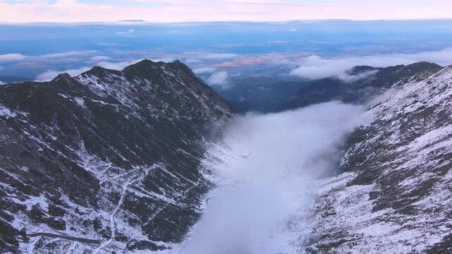 Aerial view of Transfagarasan road in Romania, in winter season. Video was shot from a drone while flying backwards at high altitude and rising the camera to reveal the horizon and the valey.