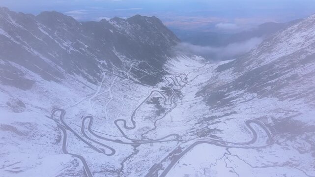 Aerial view of Transfagarasan road in Romania, in winter season. Video was shot from a drone while orbiting at high altitude through the fog with the road and the valey in the view.