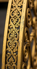 Close-up detail of ornate golden scrollwork on an old weathered architectural element, showcasing intricate classical patterns.