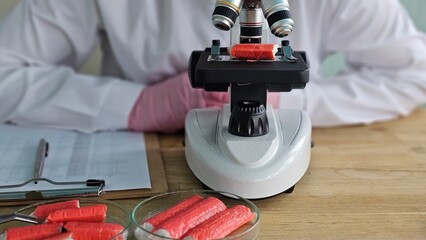 A scientist examines red samples or crab sticks under a microscope. The crab sticks were quality tested concept