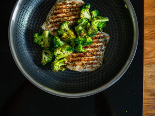Grilled pork loin steaks and broccoli in frying pan on electric stove. Top view