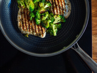 Grilled pork loin steaks and broccoli in frying pan on electric stove. Top view