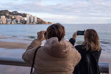 Two tourists taking photos with their mobile phones in Benidorm