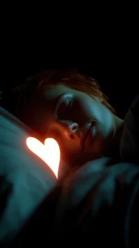 Glowing white heart symbol light on pillow near sleeping woman