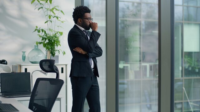 African American business man businessman male guy worker in office near window with hand on glass feeling stressed thoughtful corporate suffering from anxiety pressure thinking worried work lost