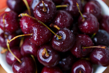 A mound of ripe cherries with stems lies in a fruit bowl. The fruits are red to dark red, covered...