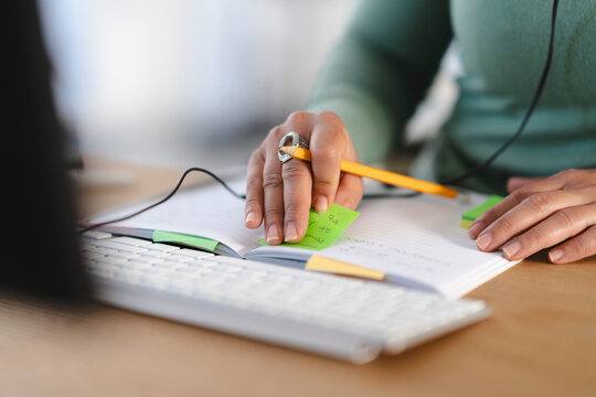 A person's hands are shown working at a desk, with a notebook, pencil, and keyboard.