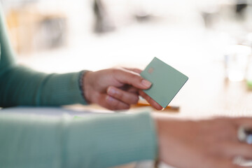 A person holds a payment card, ready to make a transaction. The card is light green with a silver logo.