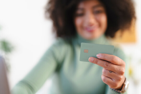 A person holds a payment card, ready to make a transaction. The card is green with a chip and embossed text.