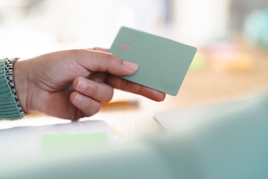A person holds a payment card with a chip and a contactless payment symbol. The card is a light green color with a silver logo.