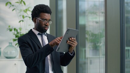 Concentrated focused African American businessman in office using digital tablet analyze data project with wireless computer technology business man guy male employer working online internet task