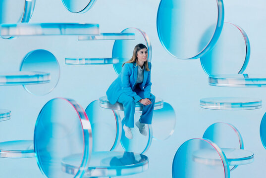 Woman sitting on floating 3D glass objects in studio scene