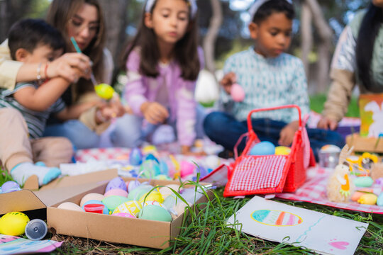 Family members and friends decorating colorful easter eggs together on a picnic blanket outdoors