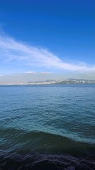 tranquil turquoise water with gentle waves and shallow ripples near shoreline, distant green hills under bright blue sky, soft