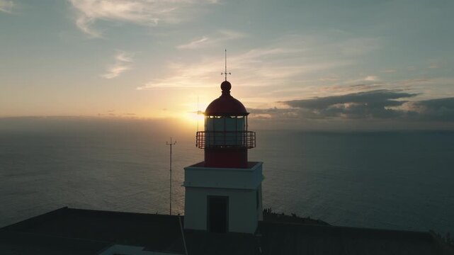 Aerial drone footage of Farol da Ponta do Pargo, a red and white lighthouse on the western coast of Madeira, Portugal. The video captures a smooth lateral flight around the lighthouse 
