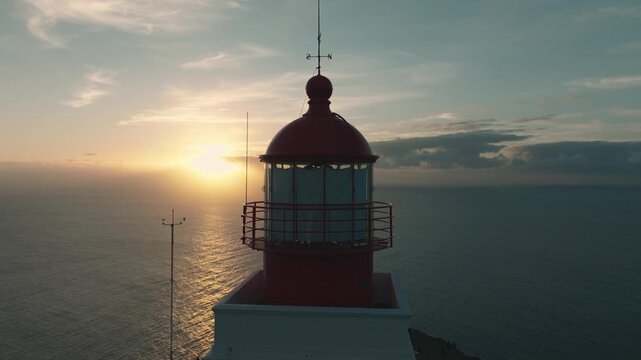 Aerial drone footage of Farol da Ponta do Pargo, a red and white lighthouse on the western coast of Madeira, Portugal. The video captures a smooth lateral flight around the lighthouse 