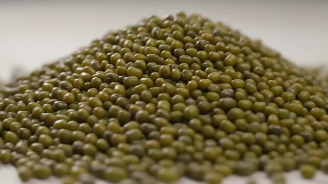 A closeup shot of a large pile of green mung beans showcasing their texture and natural color ready for cooking or sprouting.