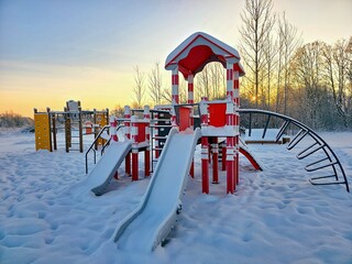 A children's playground with a slide, covered in snow, on a winter evening