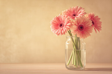 Soft pink gerbera daisies arranged in a clear glass jar on a wooden table, pastel still life floral bouquet perfect for home decor and greeting cards