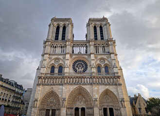 The Notre-Dame Cathedral facade in Paris, France, highlighting the intricate portals, the Gallery of Kings, the iconic rose window and two massive bell towers against a dramatic sky