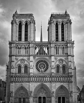The Notre-Dame Cathedral facade in Paris, France. Black and white view of the intricate portals, the Gallery of Kings, the iconic rose window and two massive bell towers against a dramatic sky