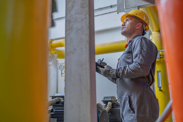 Asian engineer wearing glasses working in the boiler room,maintenance checking technical data of...