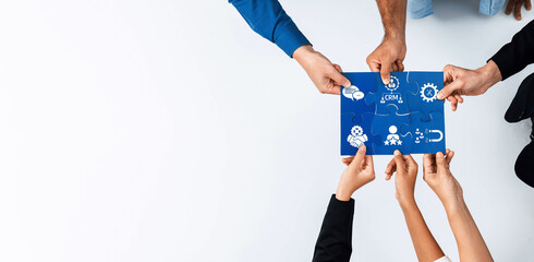 A diverse group of hands collaboratively engaging with a blueprint featuring CRM icons, symbolizing teamwork and strategic planning for business growth and innovation. Amity