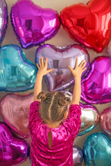 Fototapeta premium A girl in a bright purple dress decorates the wall with heart-shaped balloons for Valentine's Day