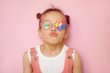 A child with a decorated lens made of stickers of multicolored puzzle pieces blows a kiss. World Autism Awareness Day