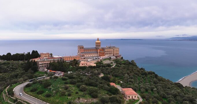 Aerial view of Sanctuary of Tindari, perched atop a hill, with a winding road leading up and the sea stretching beyond, Tindari, Sicily, Italy.