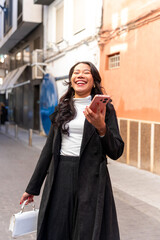 Latina businesswoman laughing while using smartphone in city