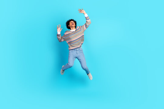 Young man jumps in a colorful sweater against a blue background for lifestyle and fashion stock photo