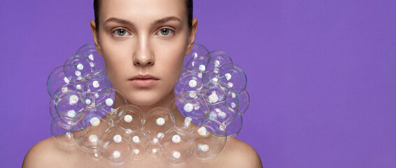 Surreal fashion portrait of young model wearing a soap bubble collar. High-end beauty concept with clean skin and electric lavender background. Creative artistic makeup and skincare.