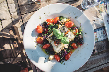 Delicious dish with vegetables and fish served on a wooden table in a bright outdoor setting during lunch time