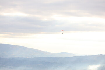 A view of the Umbrian countryside, Italy. Plains, mountains, and a cloudy sky. A hang glider in flight.