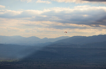 A view of the Umbrian countryside, Italy. Plains, mountains, and a cloudy sky. A hang glider in flight.