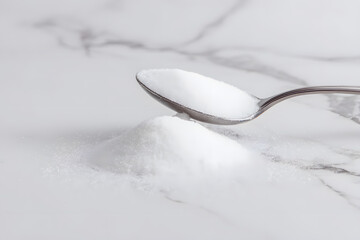 Spoonful of sugar on marble surface, showing details of texture and shine during bright lighting