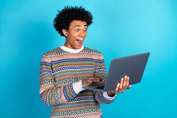 Young man in colorful sweater surprised while using laptop against blue background